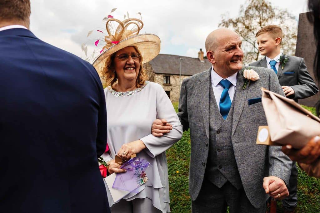 Joyful wedding celebration with guests dressed elegantly, outdoors, smiling, and wearing floral accents, capturing precious moments at a picturesque venue.