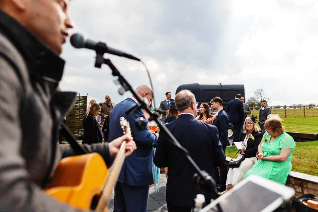 A vibrant outdoor wedding celebration with live acoustic music, guests in formal attire, and scenic rural surroundings, capturing joyful moments at BGS Weddings for memorable wedding events.