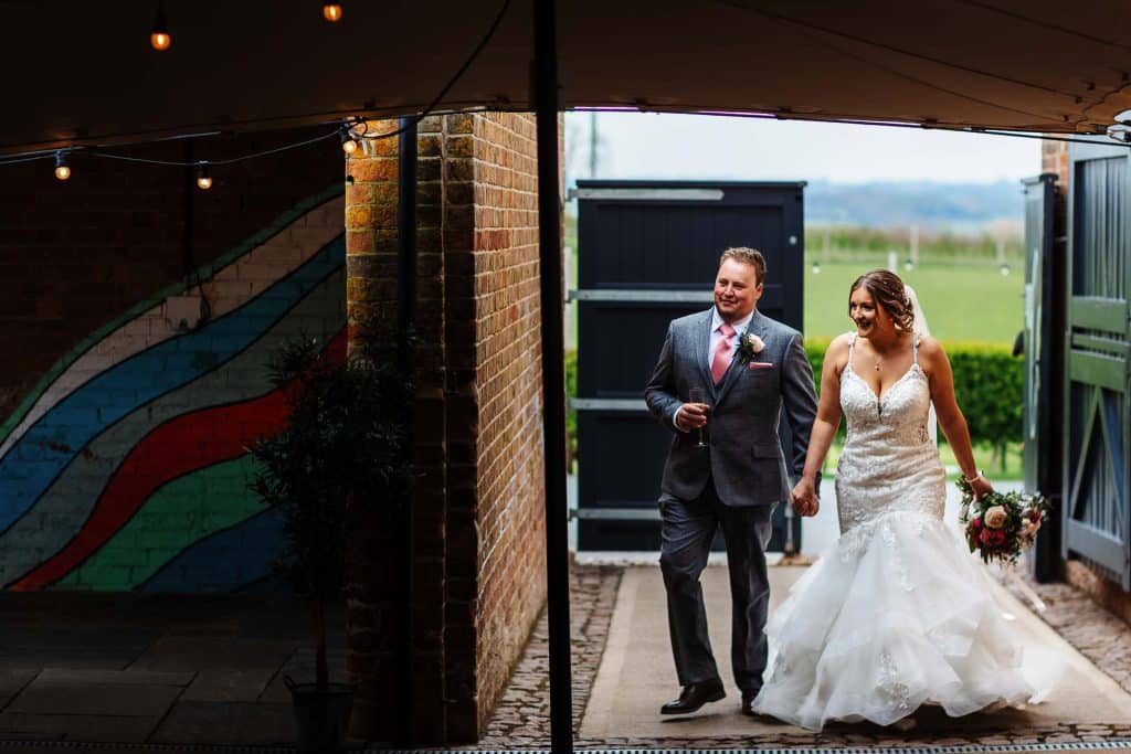 Elegant bride and groom walking hand in hand after wedding ceremony at BGS Weddings, celebrating love and happiness, with lush green background and stylish attire, perfect for wedding photography.