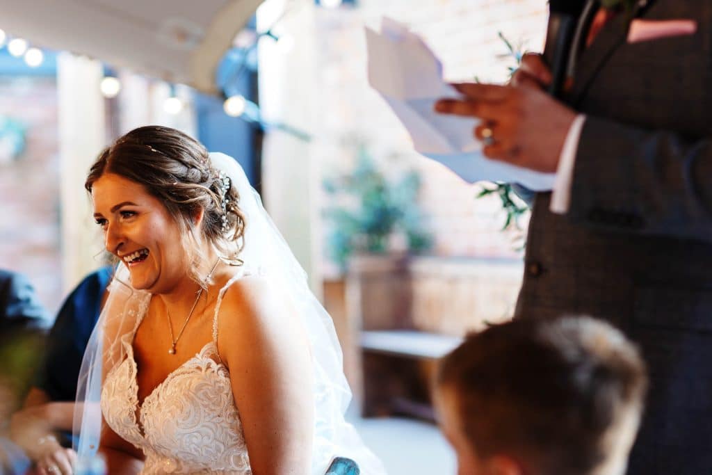 Elegant wedding bride with joyful expression, getting ready or listening to vows, in a stylish dress and veil at BGS Weddings.