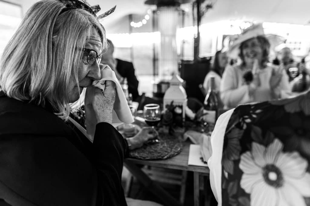 Emotional woman wiping tears at wedding reception, capturing heartfelt Moment of bride and guests, candid moment at wedding celebration, memorable day at BGS Weddings UK.
