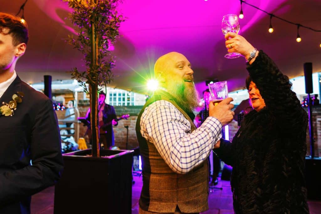 Vibrant wedding reception with guests enjoying drinks and dancing in colourful, ambient lighting, showcasing joyful celebration and lively atmosphere at BGS Weddings.