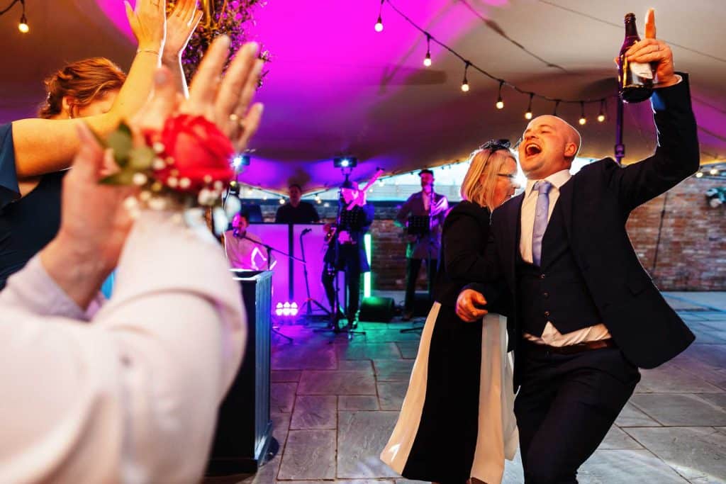 Vibrant wedding reception with guests dancing and celebrating under colourful string lights, live band performing, lively atmosphere at BGS Weddings event venue in the UK.