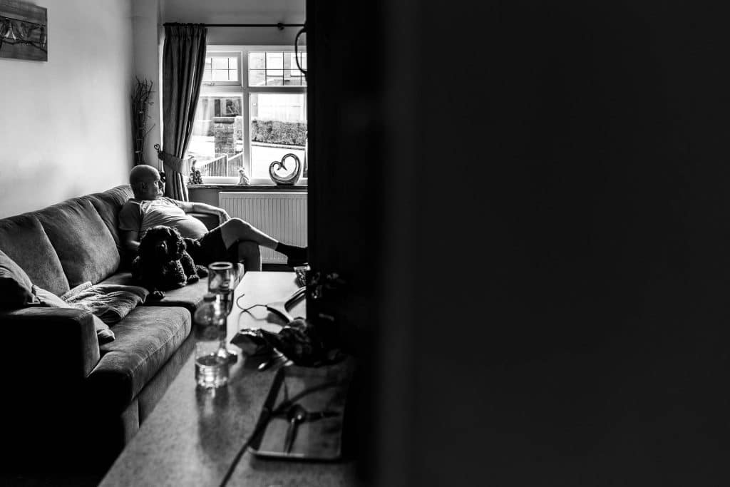 Man relaxing with dog on sofa in living room before wedding at BGS Weddings, UK; cosy, intimate moment captured in black and white.