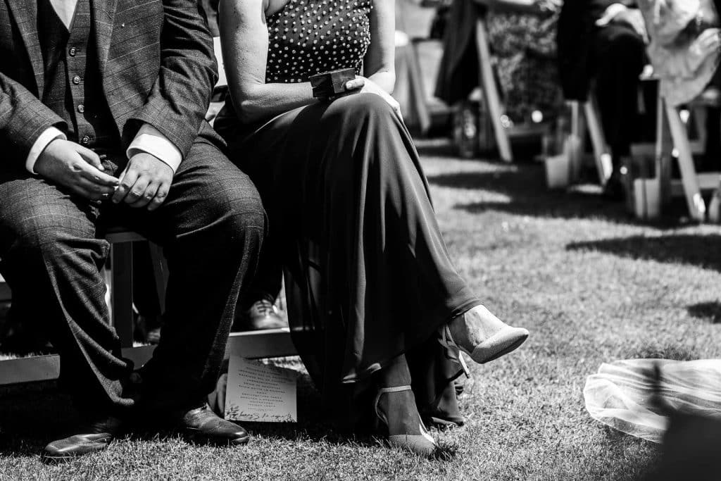 Elegant wedding ceremony, guests seated outdoors, black and white photo capturing formal attire, emotional moment, decorated venue, cherished memories, wedding celebration, BGS Weddings UK, outdoor wedding photography, special day.