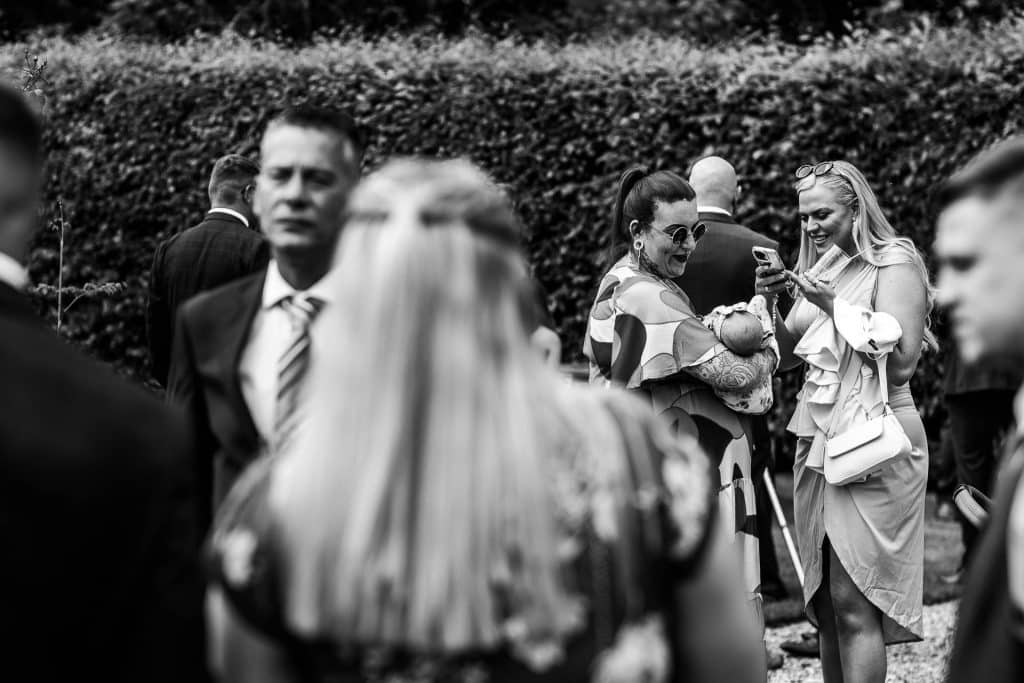 Elegant wedding guests socialising outdoors, some using smartphones, at a stylish garden wedding venue by BGS Weddings.