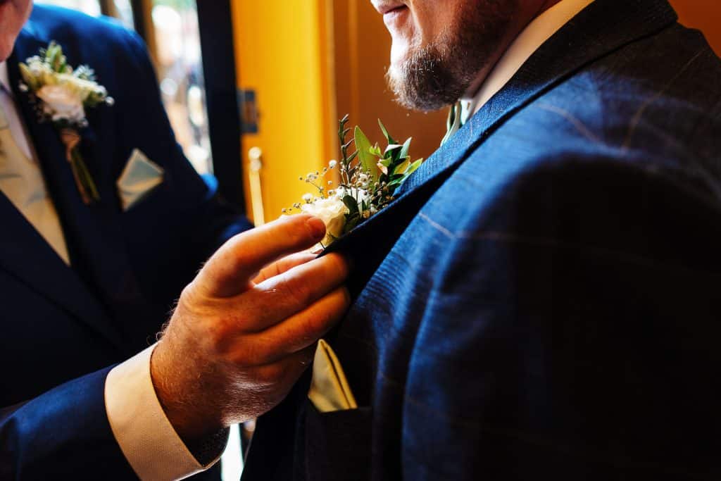 Elegant groom pinning a white floral boutonniere on his navy blue suit at a wedding.