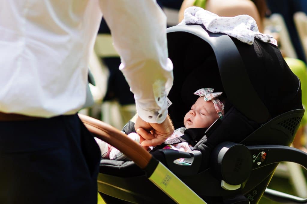 Delicate baby in a car seat at a wedding, with a person gently holding their hand, showcasing a tender moment perfect for wedding and family photography.