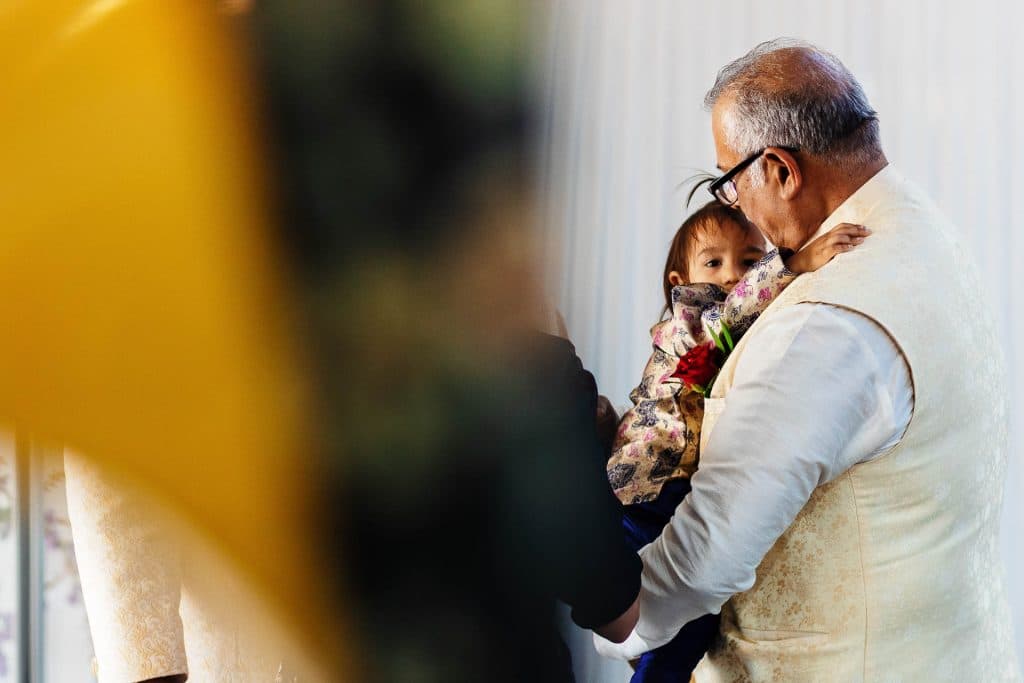 Elegant elderly man embracing a young girl dressed in traditional Indian attire at a wedding celebration, capturing a heartfelt moment of family love and cultural tradition, with focus on deep emotional connection.