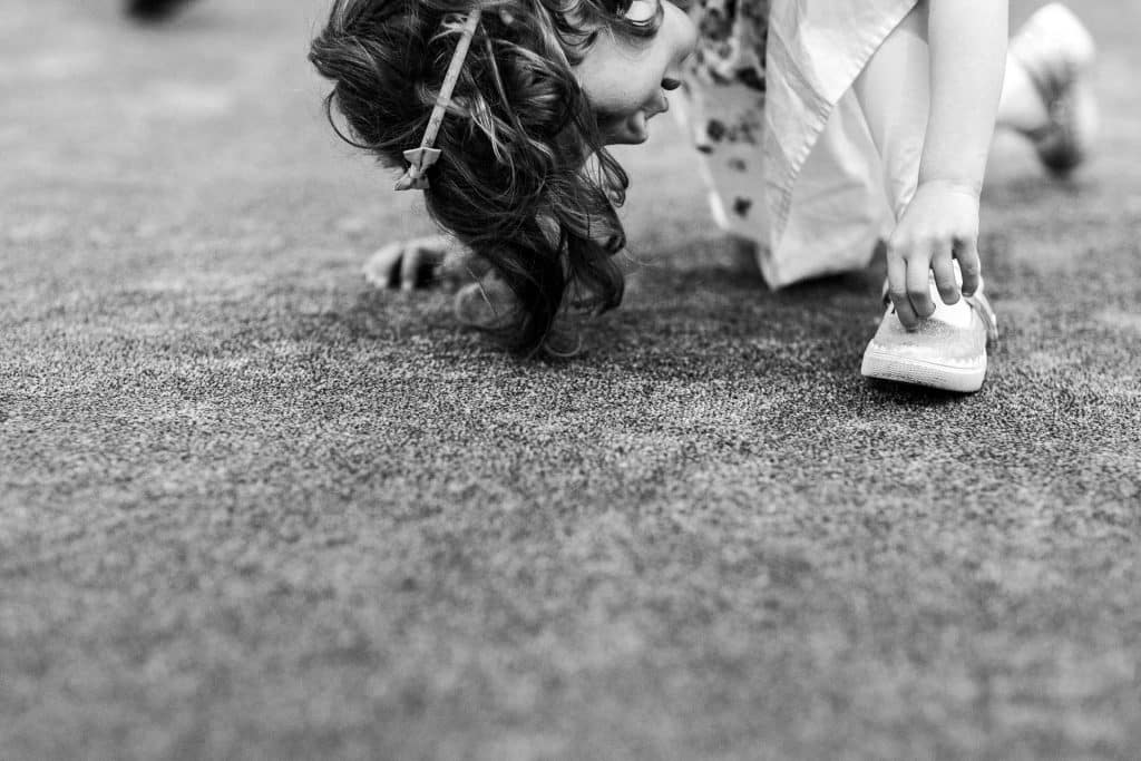 Child playing on the ground, crouched down touching her shoe, outdoor setting, black and white.