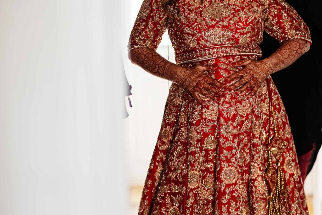 Intricate red and gold traditional wedding dress with detailed embroidery and henna designs on the bride's hands, showcasing Indian wedding attire for special ceremonies.