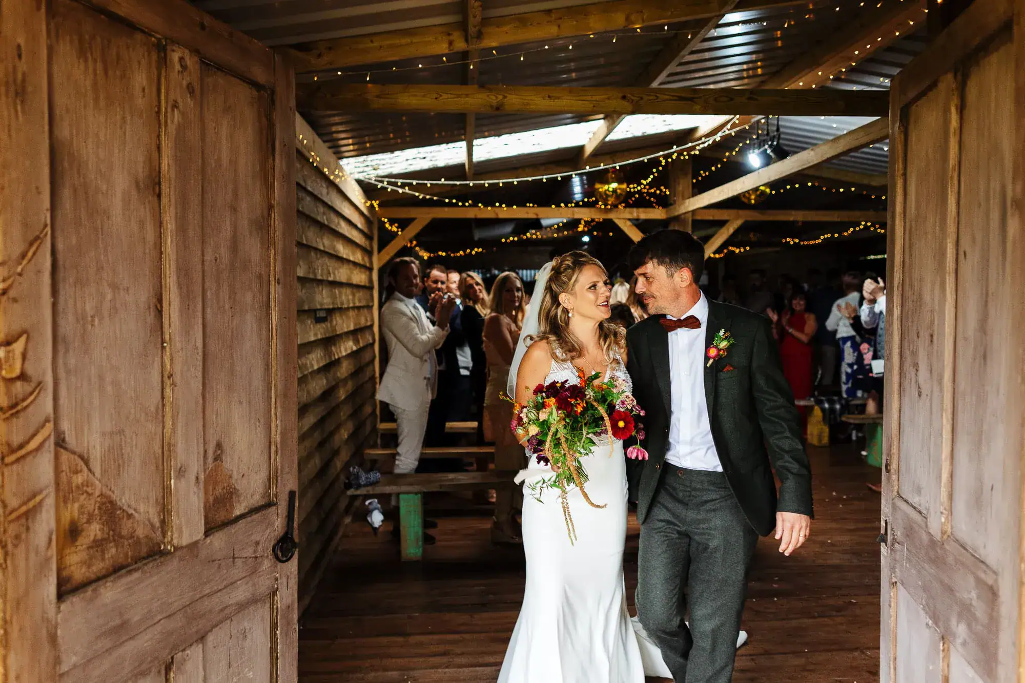 Elegant bride and groom sharing a special moment at their wedding celebration in a rustic barn setting, surrounded by joyful guests, warm lighting, and romantic floral arrangements.