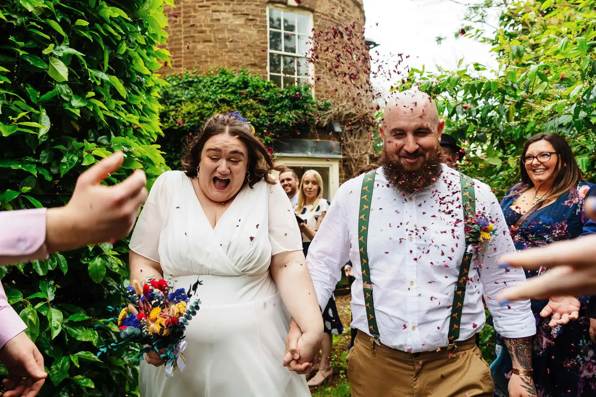 Joyful wedding celebration with confetti shower, happy bride and groom holding hands, surrounded by friends and family in a lush garden setting, capturing a vibrant and festive moment.