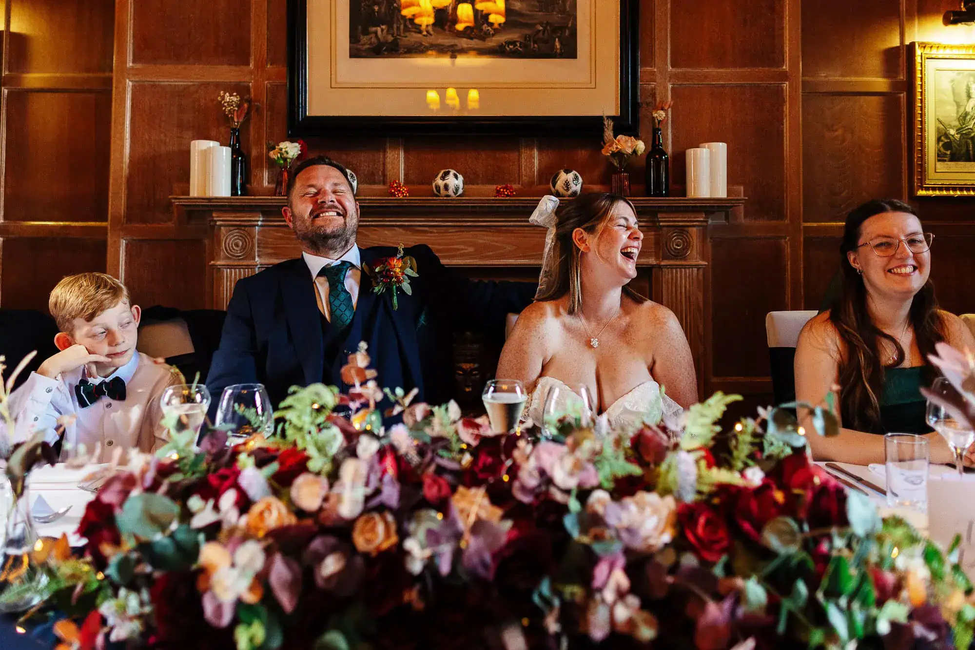 Elegant wedding reception celebration with joyful bride, groom, and guests seated at a beautifully decorated table, capturing a moment of happiness and laughter at a traditional wedding venue.