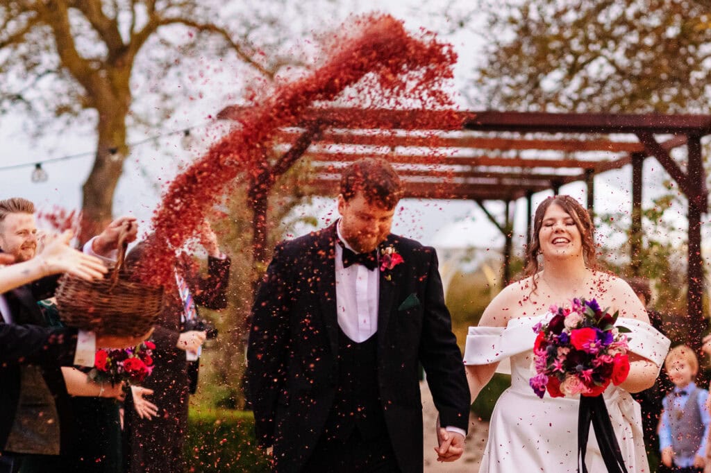 Vibrant wedding celebration at BGS Weddings with newlyweds being showered with confetti, outdoor ceremony, romantic atmosphere, elegant dress, and joyful first moments after the wedding.