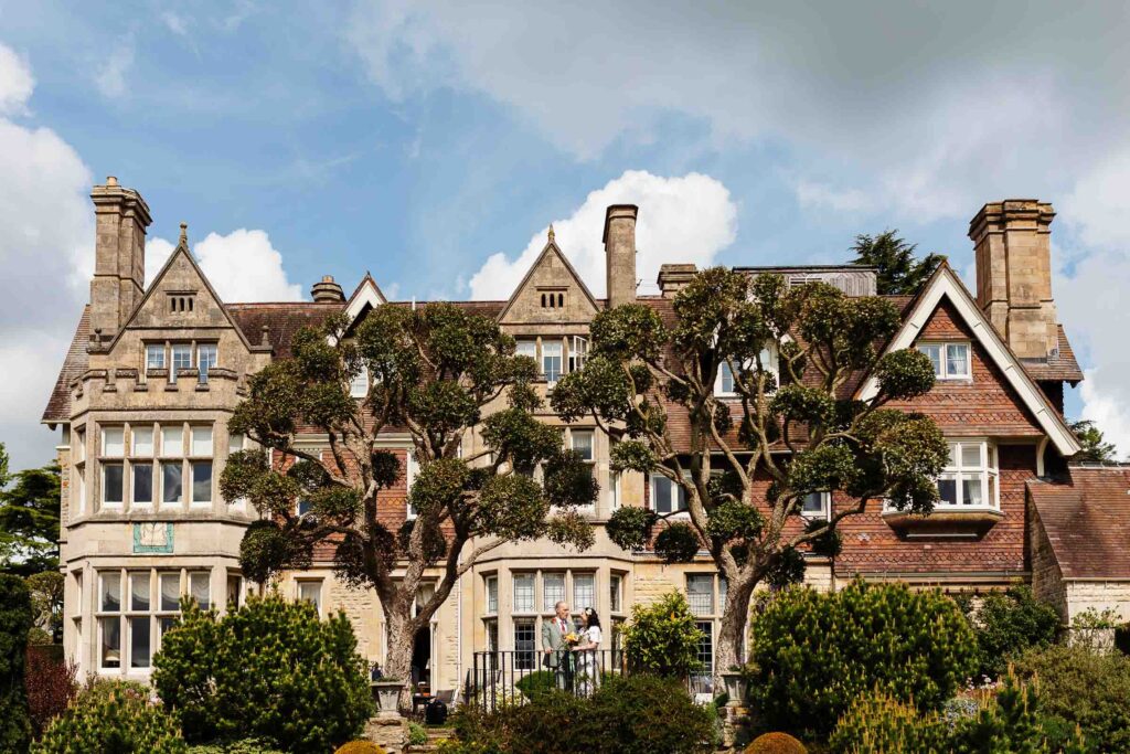 Stunning wedding ceremony outdoors at a historic UK estate, featuring a beautiful grand hotel, lush gardens, and classic Tudor-style architecture. Perfect wedding venue in the UK.