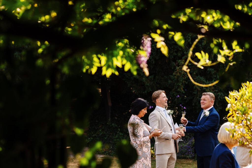 Elegant wedding celebration outdoors at BGS Weddings, showcasing joyful guests raising glasses in a beautiful garden setting with lush greenery and sunlight.