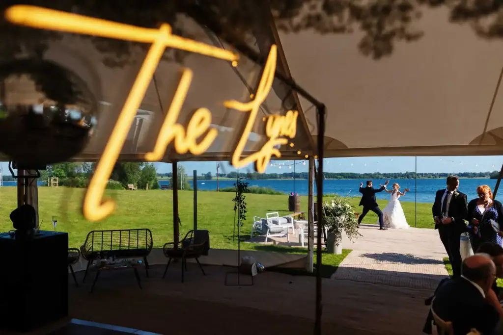 Elegant outdoor wedding reception beside a scenic lake with dancing and joyful guests, captured by BGS Weddings to showcase beautiful UK lakeside wedding venues and event planning services.