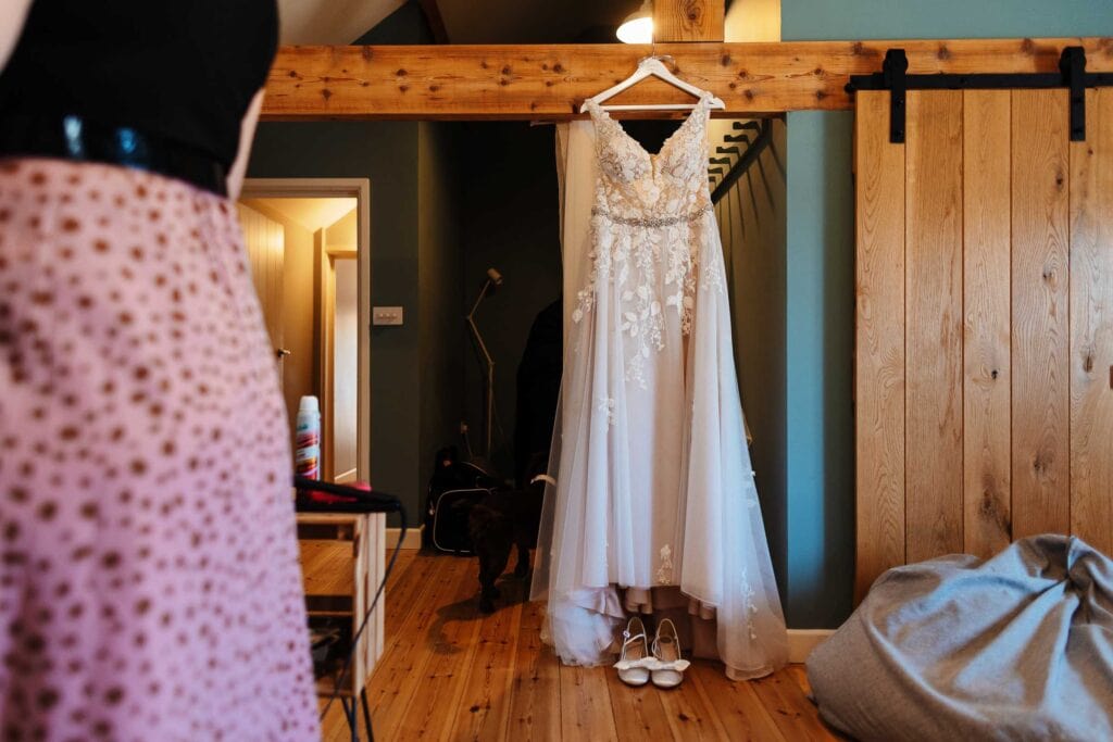Elegant wedding dress hanging on a wooden rack, with bridal shoes placed underneath, in a cozy bridal preparation room. Perfect for capturing wedding day moments and wedding dress details.
