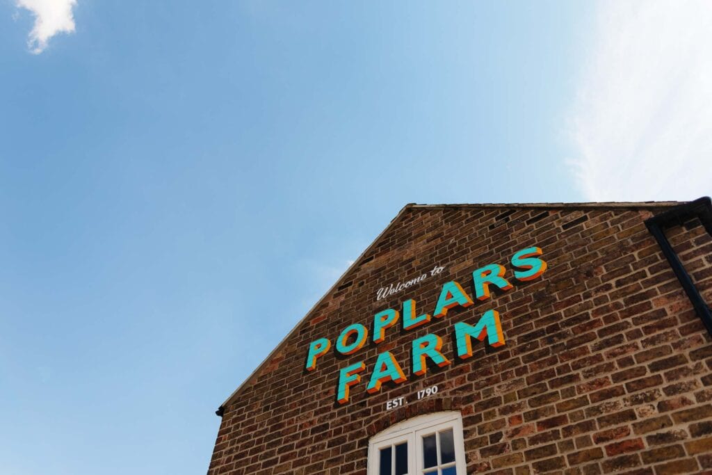 Vibrant Poplars Farm wedding venue sign on a historic brick building with a bright blue sky, ideal for wedding photography and event planning in Kent.