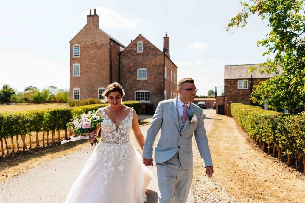 Elegant bride and groom walking hand in hand outside historic wedding venue, capturing romantic wedding day moments at BGS Weddings in the UK.