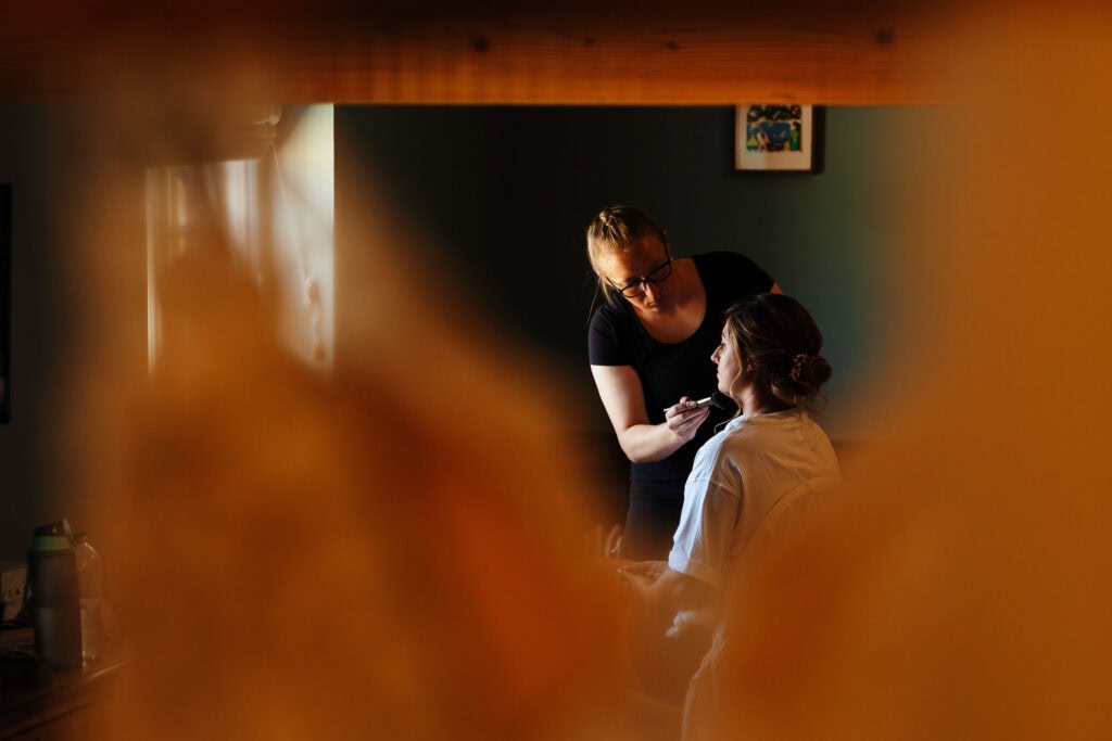 Brighton wedding makeup artist applying makeup to bride in a warmly lit, stylish boutique setting. Bridal hair and makeup services, expert wedding makeup artist, professional bridal beauty.