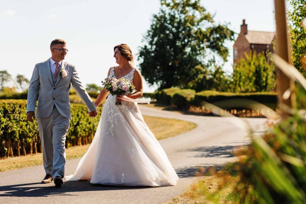 Elegant bride and groom holding hands walking outdoors during wedding ceremony at BGS Weddings, showcasing romantic wedding photography, beautiful scenery, and outdoor wedding decor.