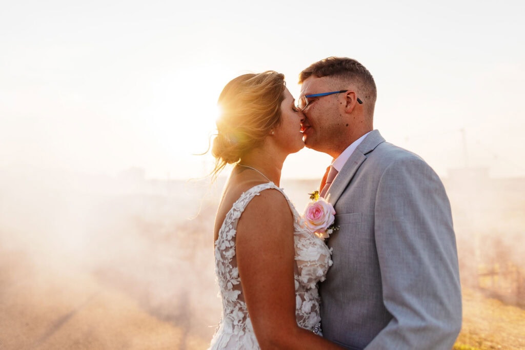 Elegant bride and groom sharing a kiss at sunset, capturing romantic wedding photography for BGS Weddings in the UK, highlighting natural light and emotional moments.