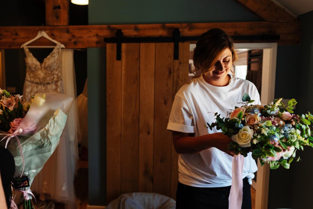 Beautiful woman preparing wedding bouquet in rustic bridal preparation room at BGS Weddings, showcasing bespoke wedding flowers and event styling services in the UK.