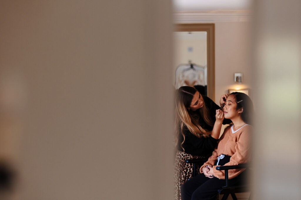 Elegant bride getting her makeup done by a professional makeup artist in a luxurious hotel room, captured in a candid moment before her wedding. Perfect for wedding, bridal, and beauty services SEO.