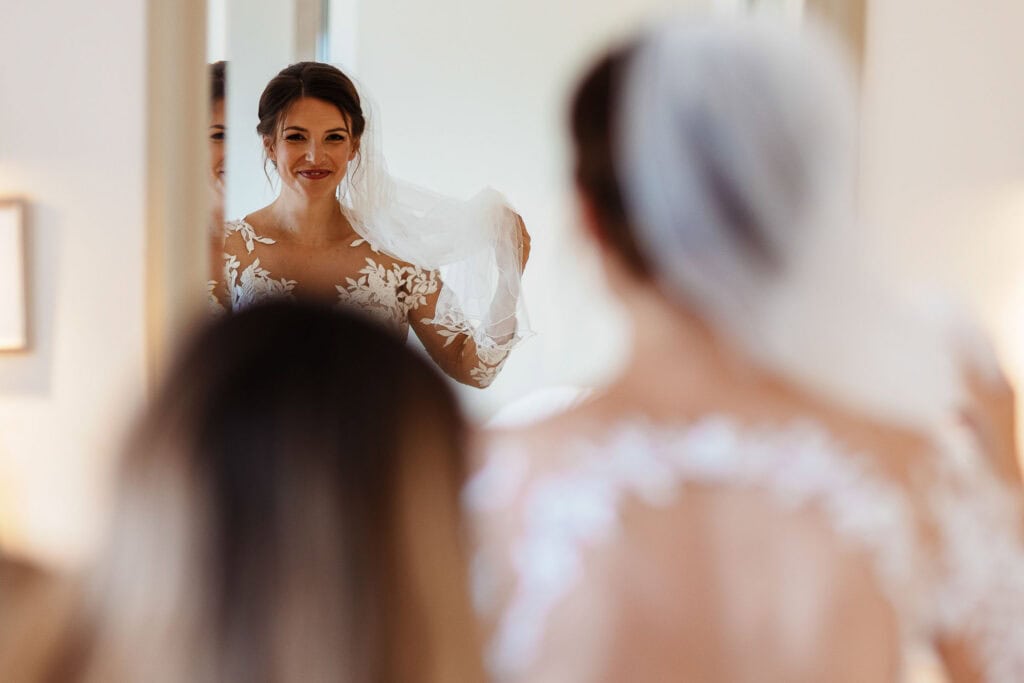 Elegant bride smiling at herself in the mirror, ready for her wedding day, showcasing beautiful bridal gown and accessories for a perfect wedding celebration.