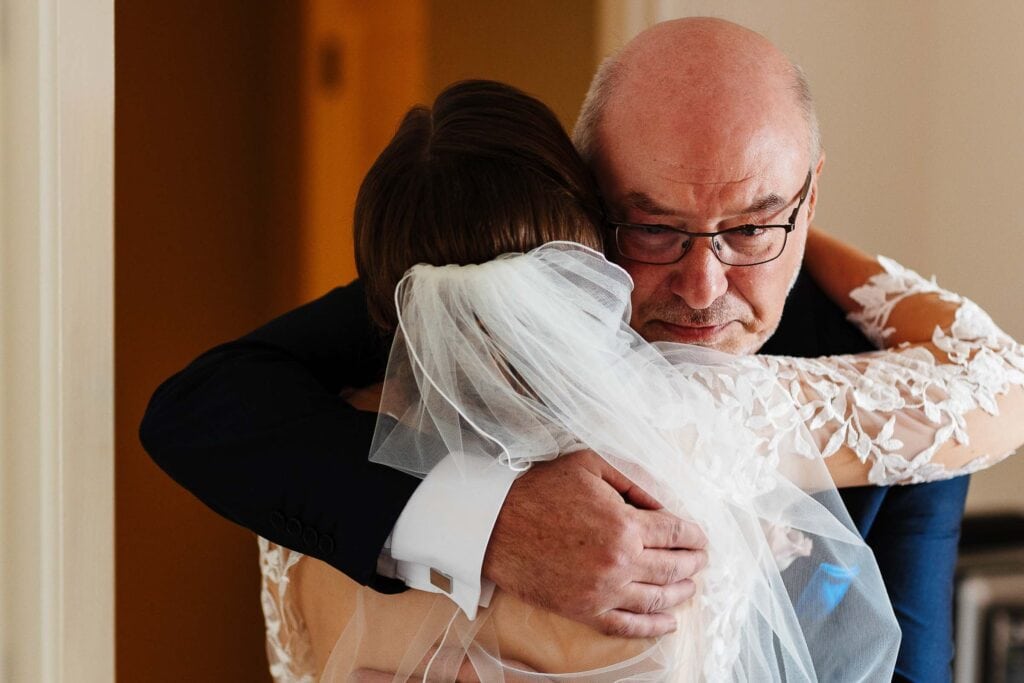 Emotionally heartfelt father-daughter wedding day hug in a bridal gown and tuxedo, capturing tender family moments, perfect for wedding photography and wedding day memories.