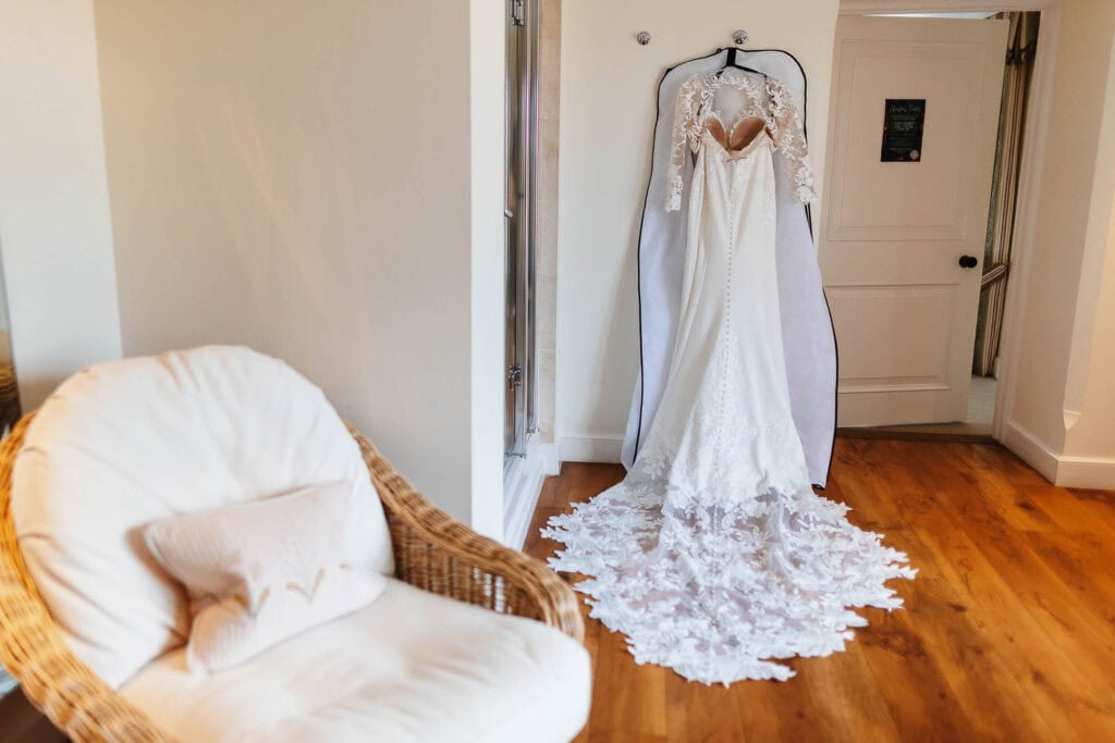 Elegant wedding dress hanging on a door chandelier with lace details, ready for a bride on her wedding day at BGS Weddings in the UK.