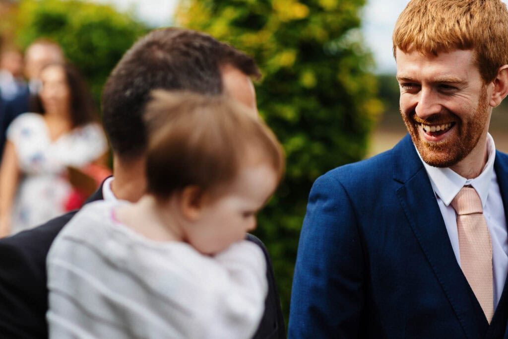 Brighton wedding photographer capturing joyful moments at outdoor wedding in Sussex, featuring happy groomsman and guests in elegant attire, beautiful natural setting, and celebratory atmosphere.