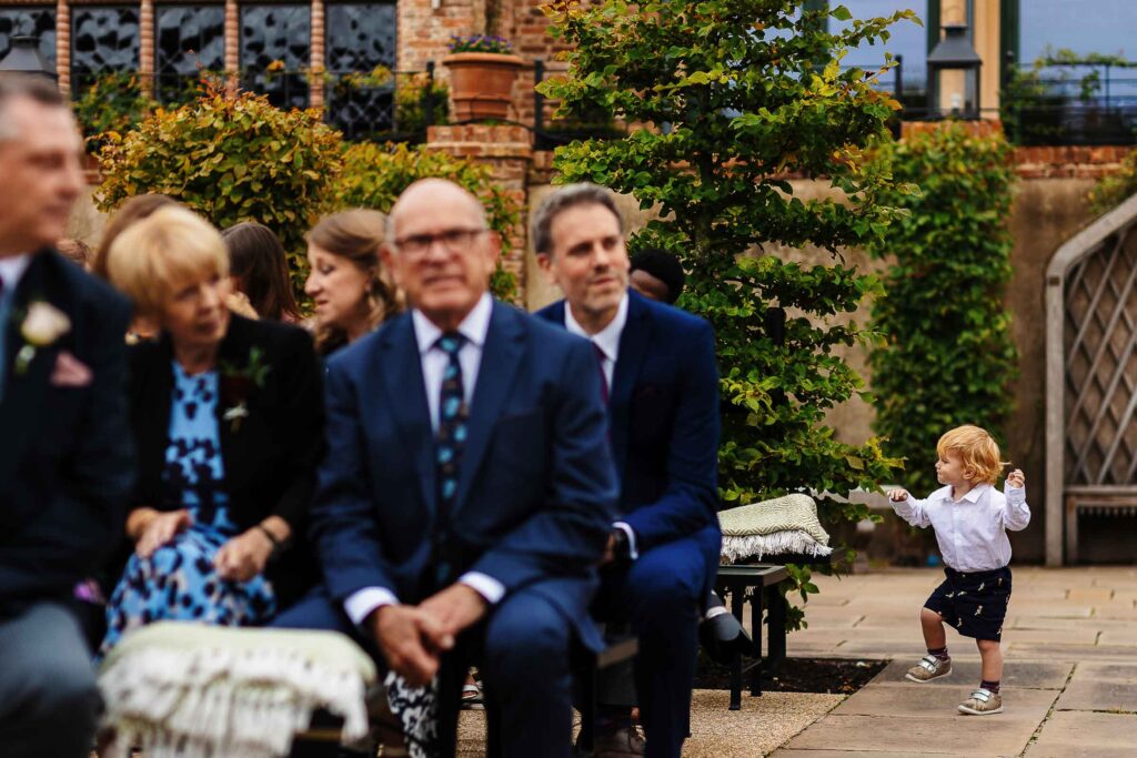 A happy outdoor wedding ceremony at BGS Weddings, featuring elegantly dressed guests seated on benches, lush greenery, and a charming garden setting.