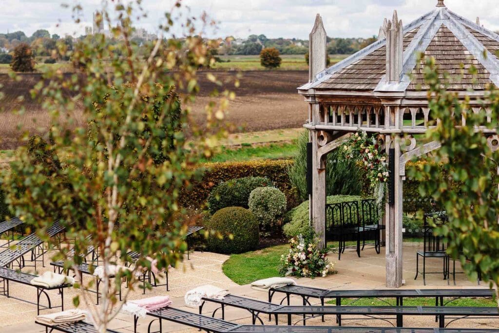 Beautiful outdoor wedding ceremony area at BGS Weddings featuring a wooden pagoda decorated with flowers in a scenic countryside setting.