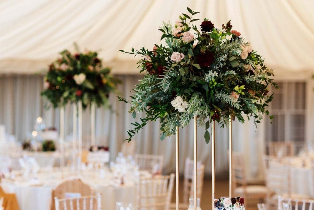 Elegant floral wedding centrepiece featuring lush greenery and blush pink and deep burgundy flowers at a wedding reception. Perfect for decorating wedding tables with sophistication.
