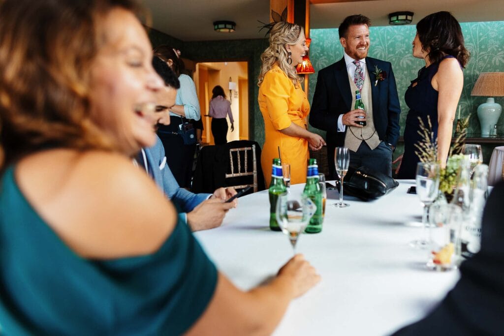 Elegant wedding guests enjoying conversations at BGS Weddings in a beautifully decorated venue with drinks and floral centrepieces.