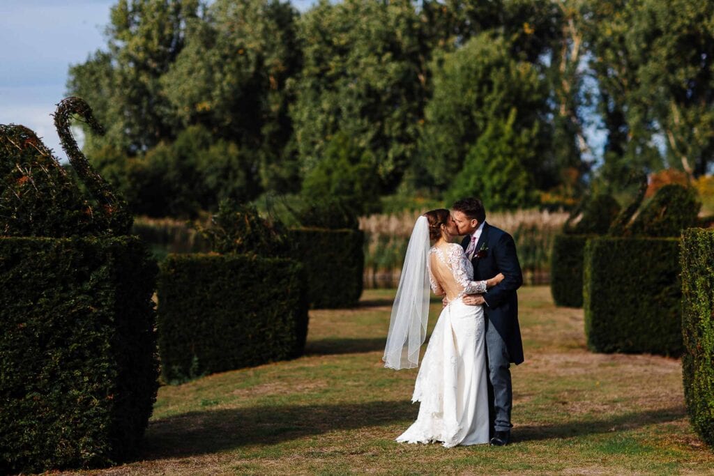 Beautiful newlywed couple sharing a romantic kiss in a lush garden, perfect for outdoor wedding photography. Elegant wedding attire, stunning natural setting, ideal for wedding photoshoots.