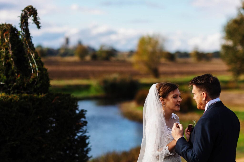 Elegant wedding couple exchanging vows outdoors at a scenic countryside location with a river and trees, ideal for wedding photography and natural wedding venues in the UK.