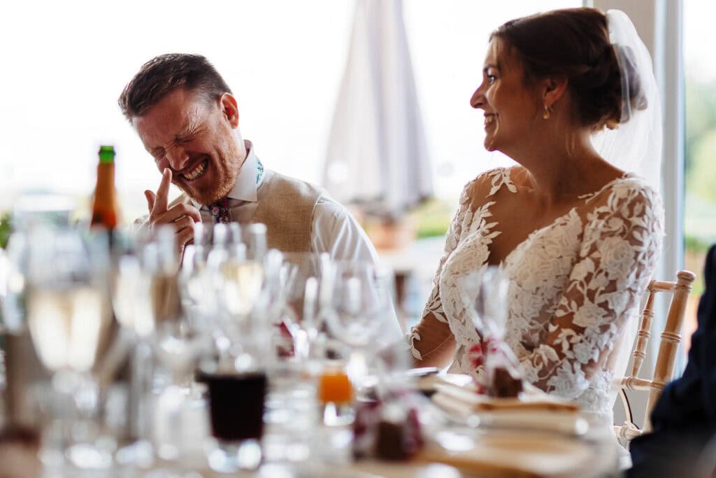 Laughter and joy at a wedding reception, bride and groom enjoying a happy moment. Elegant wedding celebration with guests, foodie decor, and natural light in a beautiful venue. Perfect for wedding photography.
