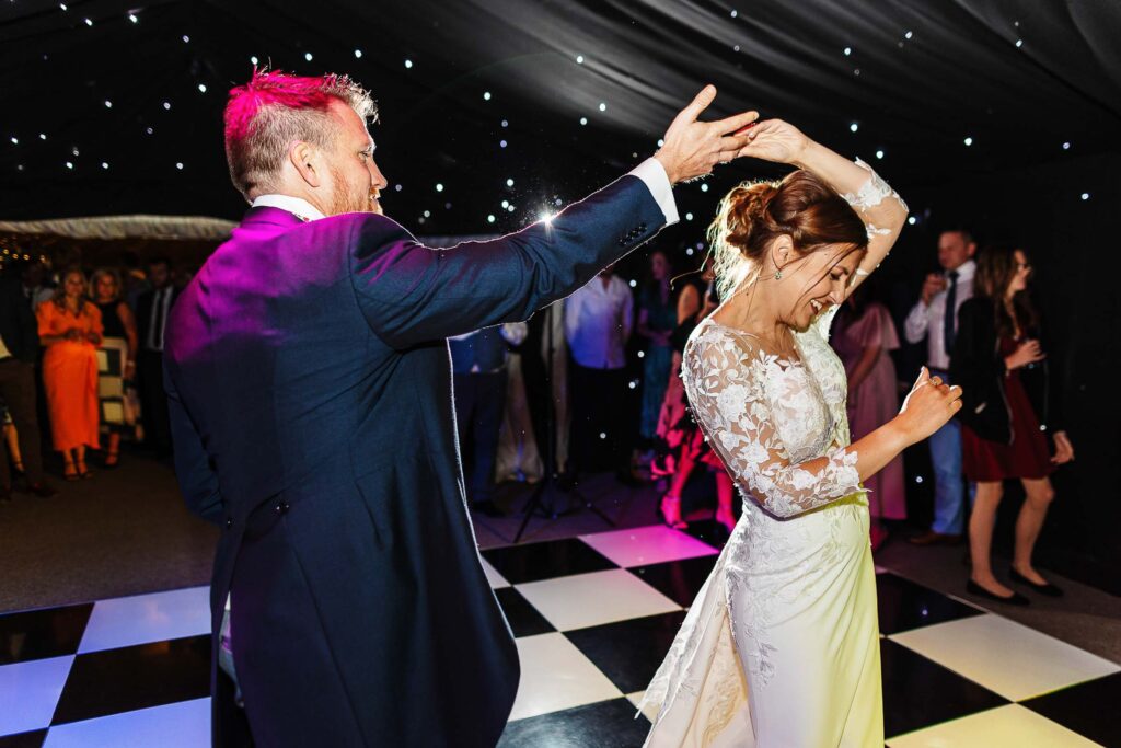 Elegant groom and bride dancing at wedding reception under starry ceiling, lively atmosphere, joyful couple, wedding celebration, dancing, entertainment, BGS Weddings UK.