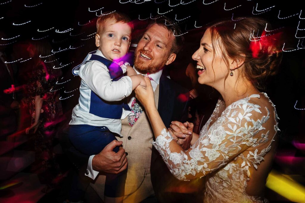 Lively wedding celebration with bride, groom, and a young boy dancing at the reception, capturing joyful moments and vibrant atmosphere.
