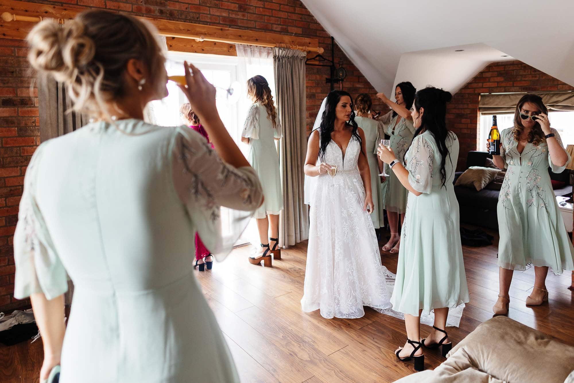 Bridge house barn wedding photographer Elegant bride preparing with bridesmaids in a cosy, rustic bridal suite, wearing matching pastel green robes, celebrating her wedding day with friends and family.