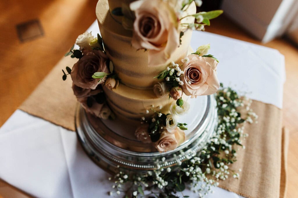 Rich pastel wedding cake decorated with fresh roses and baby's breath on a silver cake stand, perfect for elegant wedding receptions.