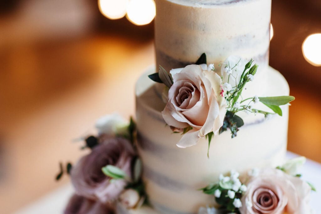 Elegant wedding cake decorated with soft pink roses and greenery, perfect for a romantic wedding celebration by BGS Weddings.