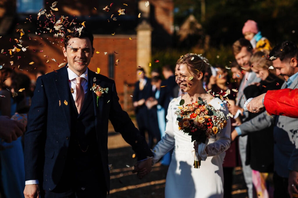 Confetti celebration at wedding, bride and groom smiling, outdoor wedding ceremony, autumn setting, wedding day happiness, BGS Weddings UK, joyful marriage celebration.