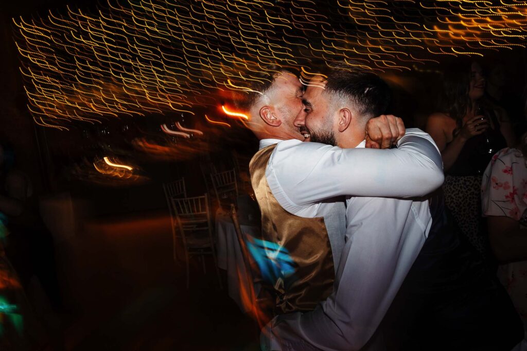 Celebrating a joyful wedding dance with a heartfelt embrace, surrounded by warm string lights and a lively atmosphere at BGS Weddings venue.
