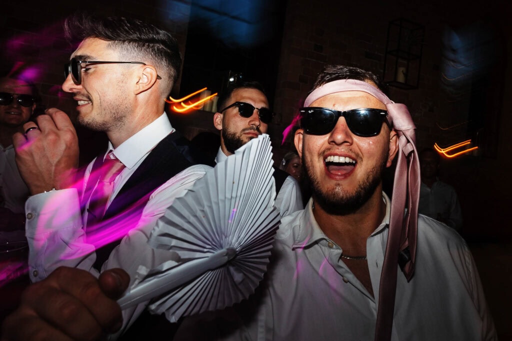 Vibrant wedding celebration with friends dancing and enjoying the party, capturing the lively atmosphere with colourful lights and fun accessories, perfect for a memorable wedding event.