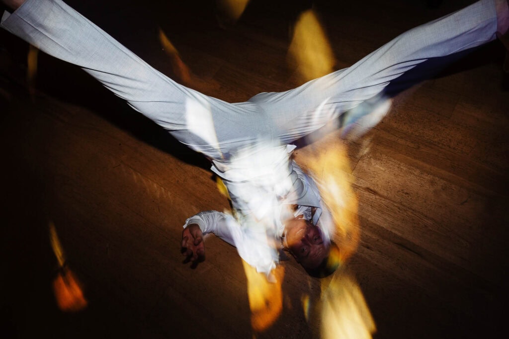 Vibrant wedding dance floor with a groom in a light grey suit spinning, illuminated by colourful lights, capturing joyful moments at BGS Weddings.